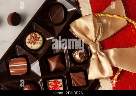 Assorted chocolates in elegant red gift pack with golden ribbon put on top of a white marble background. A stylish christmas and valentines day gift o Stock Photo