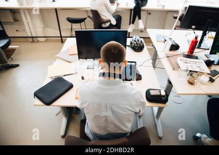 Rear view of male computer programmer using laptop on desk while sitting in creative office Stock Photo