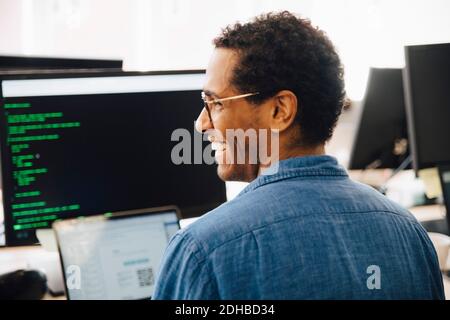 Rear view of cheerful male it professional looking away while sitting in creative office Stock Photo