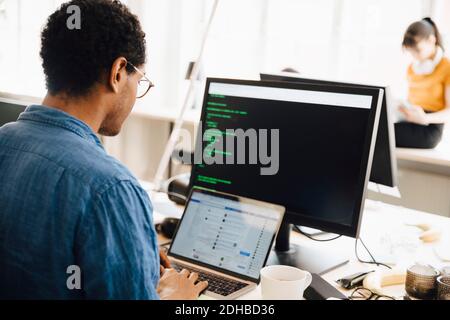Male computer hacker using laptop on desk while sitting in creative office Stock Photo