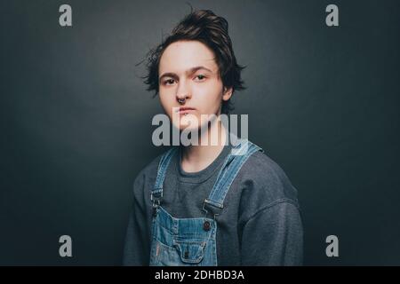 Portrait of trendy young man wearing bib overalls over colored background Stock Photo