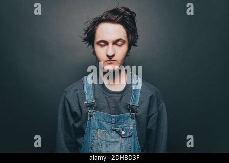 Young man with eyes closed wearing denim overalls over gray background Stock Photo