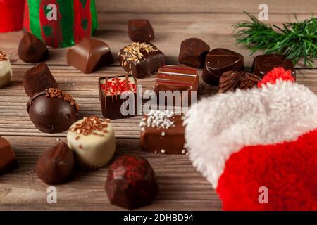 Pieces of delicious assorted chocolates are coming out of a christmas stocking on wooden table. Pine christmas tree piece with holiday gift decor are Stock Photo