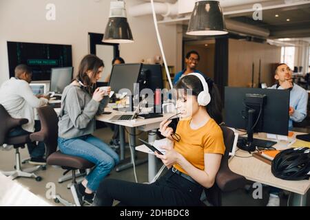 Female IT professional using digital tablet while coworkers working in background at creative office Stock Photo
