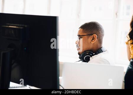 Side view of computer programmer with headphones sitting against window in office Stock Photo