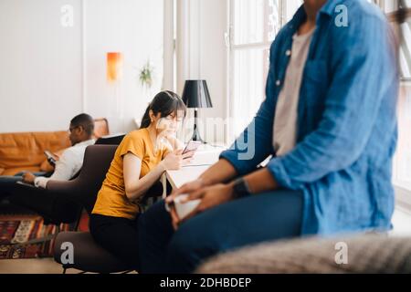 Female programmer using mobile phone on desk while sitting in office Stock Photo