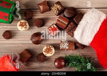Pieces of delicious assorted chocolates are coming out of a christmas stocking on wooden table. Pine christmas tree piece with holiday gift decor are Stock Photo