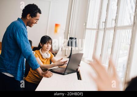 Female programmer explaining to male coworker over laptop on desk in office Stock Photo