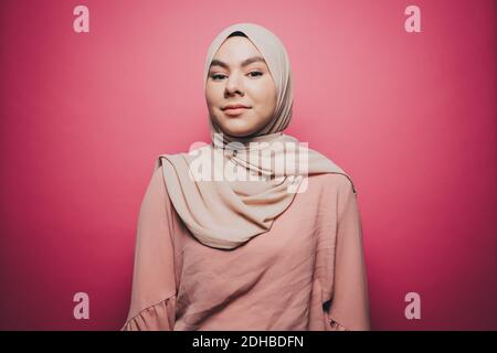 Portrait of confident young woman wearing hijab against pink background Stock Photo