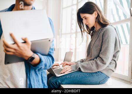 Midsection of businessman holding laptop while female programmer using laptop in office Stock Photo