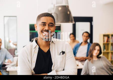 Portrait of smiling computer programmer standing with colleagues in background Stock Photo