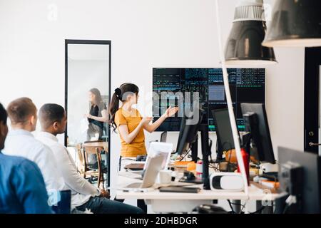 Female computer hacker presenting code on television screen during meeting with programmers in creative office Stock Photo