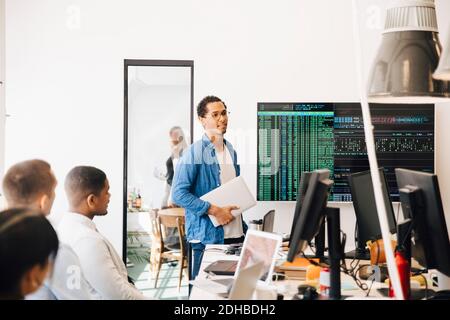 Computer hacker explaining code on television screen to programmers during meeting in creative office Stock Photo