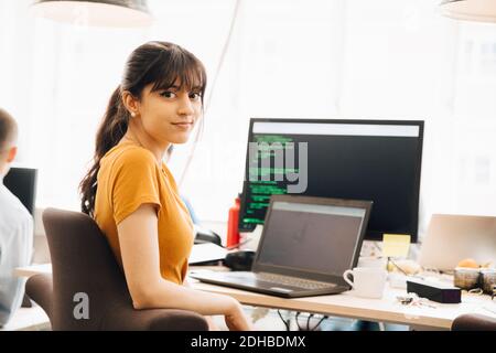 Portrait of female programmer using laptop while sitting at desk in office Stock Photo