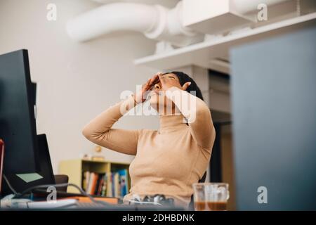 Frustrated female computer programmer with head in hands sitting in creative office Stock Photo