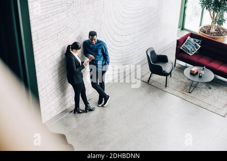 Full length of business partners talking while leaning on wall at office conference Stock Photo
