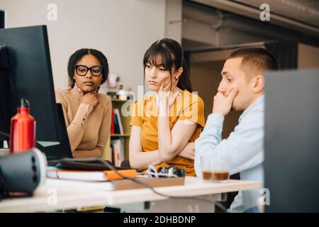 Focused computer programmers looking at laptop while working together at desk in creative office Stock Photo