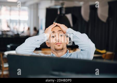 Exhausted computer programmer with head in hands looking at computer while working in office Stock Photo