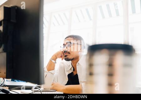 Tired computer programmer looking at computer while working in office Stock Photo