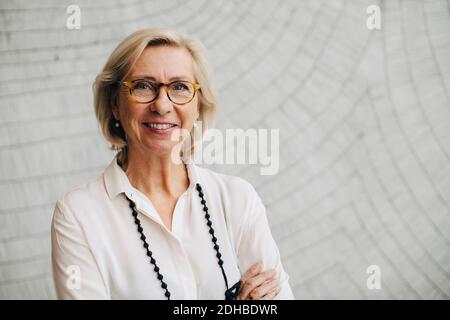 Portrait of smiling senior businesswoman standing against wall in office Stock Photo
