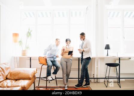 Full length of computer programmers looking at digital tablet while discussing by window in office Stock Photo