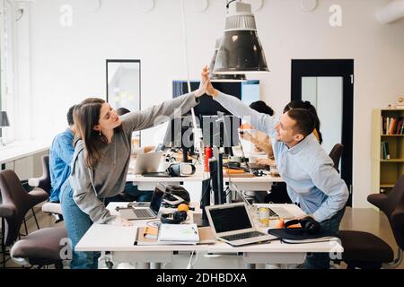 Happy male and female computer programmers doing high-five over computer at desk in creative office Stock Photo