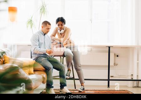 Full length of male and female hackers discussing over laptop by window in office Stock Photo