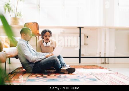 Programmers working over laptop while sitting on carpet in office Stock Photo