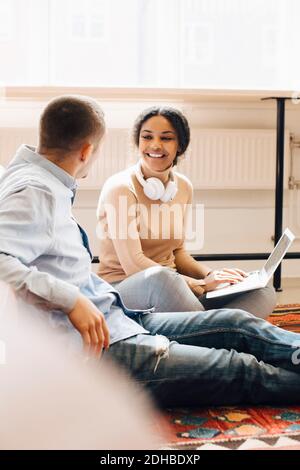Smiling female programmer looking at male colleague while using laptop in office Stock Photo