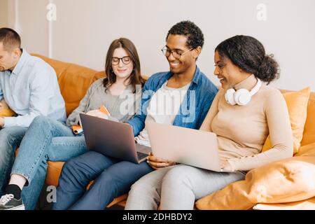 Smiling programmers working over laptops while sitting on sofa in creative office Stock Photo