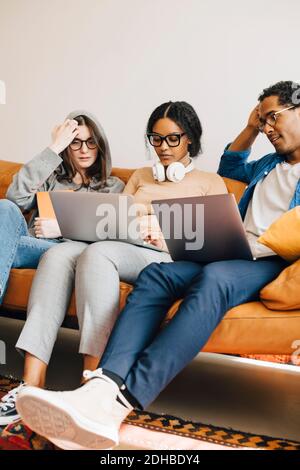 Computer programmers working on laptops while sitting on sofa in creative office Stock Photo