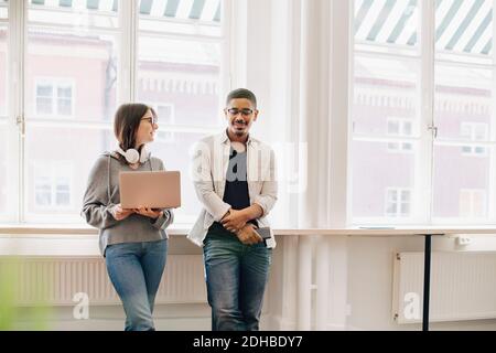 Smiling computer programmers talking while standing by desk in office Stock Photo