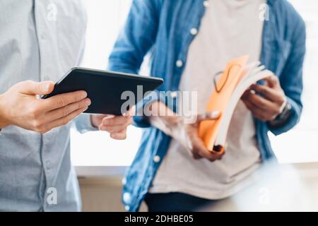 Midsection of male computer programmers with book and digital tablet standing in office Stock Photo