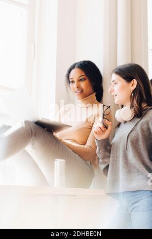 Female computer programmers discussing over laptop by window in office Stock Photo