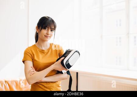 Portrait of female entrepreneur holding virtual reality simulator while standing by window Stock Photo