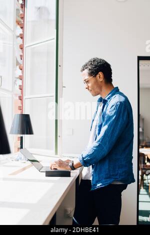 Side view of computer hacker working on laptop at desk by window in office Stock Photo