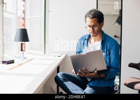 Computer programmer working on laptop while sitting by window in office Stock Photo