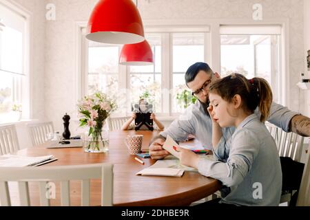 Man assisting daughter while girl using digital tablet in background at home Stock Photo