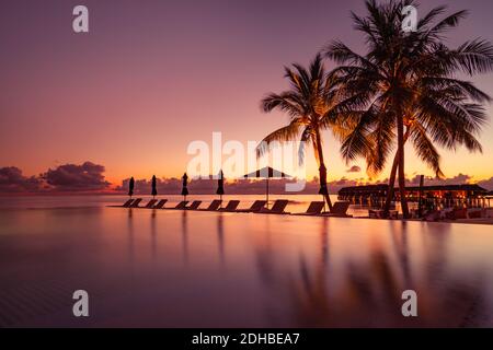 Beautiful poolside and sunset sky. Luxurious tropical beach landscape, deck chairs and loungers and water reflection. luxury swimming pool on beach Stock Photo