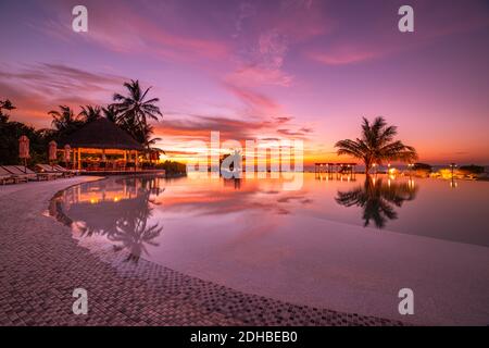 Beautiful poolside and sunset sky. Luxurious tropical beach landscape, deck chairs and loungers and water reflection. luxury swimming pool on beach Stock Photo