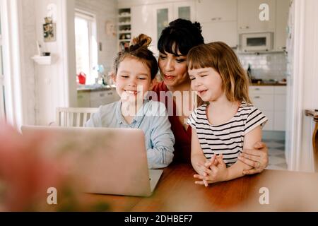 Mother and daughters looking at laptop while sitting in living room Stock Photo