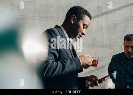 Young businessman using mobile phone while having tea at office Stock Photo