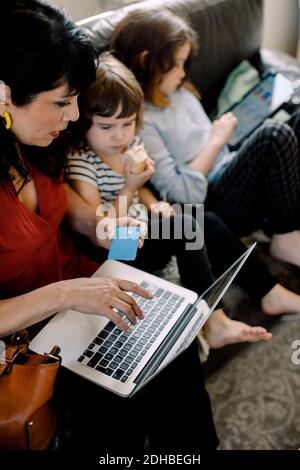 High angle view of woman doing online shopping through laptop while sitting with daughters at home Stock Photo