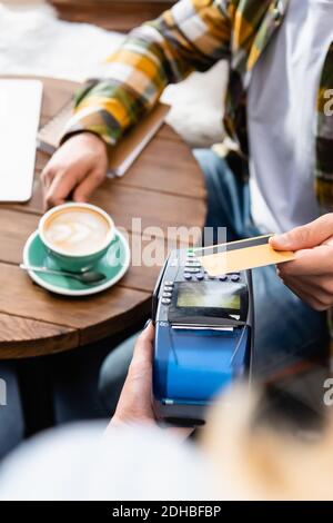 cropped view of waiter holding payment terminal and man with credit card sitting at table with cup of coffee Stock Photo