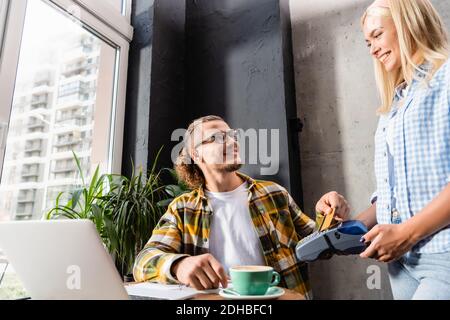 young man paying with credit card through terminal in hands of smiling waiter Stock Photo