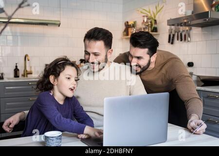 Happy fathers looking at daughter using laptop at table in kitchen Stock Photo