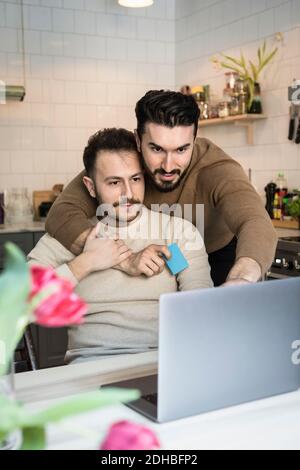Homosexual couple doing online shopping through laptop in kitchen at home Stock Photo