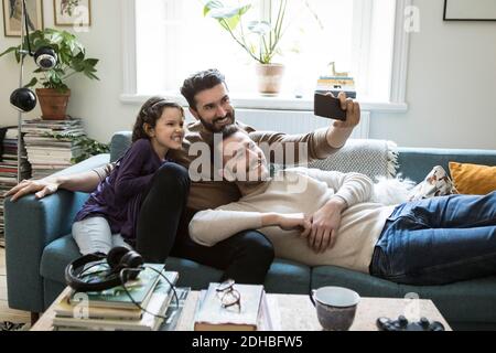 Fathers taking selfie with daughter through mobile phone on sofa at home Stock Photo