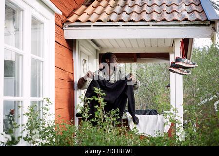Smiling young man drying clothes while standing outside cottage Stock Photo