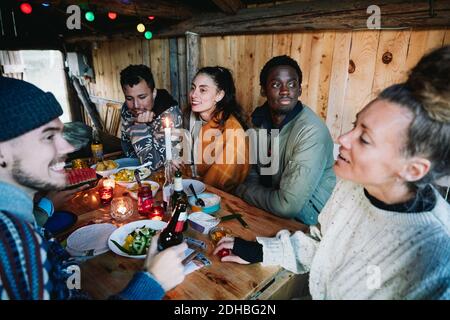 Male and female friends talking while having food on table in log cabin Stock Photo